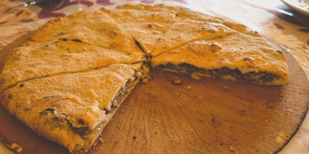 A medfouna, or Berber pizza, cut into wedges on a wooden board